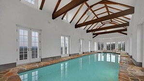 An indoor swimming pool with stone flooring, wooden beams, and large windows. - Roundtop Mansion Breathtaking View indoor Pool (Wrightsville)