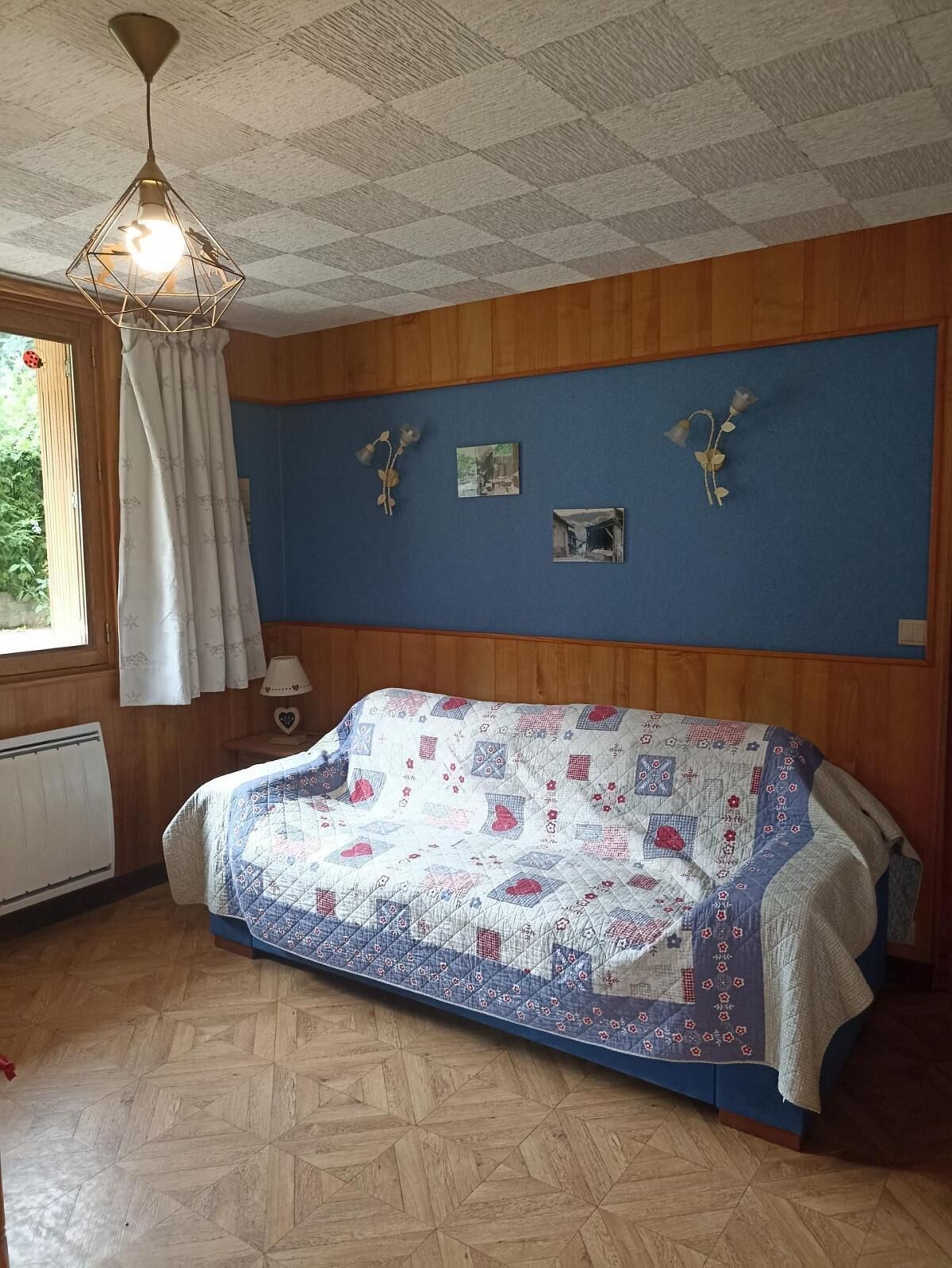 Une pièce avec un mur lambrissé en bois, un mur bleu orné de trois tableaux encadrés, un plancher en bois et un canapé bleu recouvert d’une courtepointe.