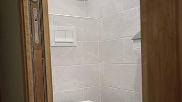 A small, enclosed bathroom with a toilet, a hand dryer, and a blue toilet brush.