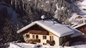 A chalet-style building with a wooden balcony, surrounded by snow-covered trees and a mountainous backdrop.