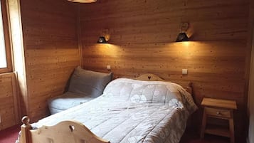 A wooden-paneled bedroom with a bed, two wall-mounted lamps, and a small bedside table.