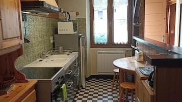 A compact kitchen with a checkered floor, wooden cabinets, a built-in oven, and a window with lace curtains.