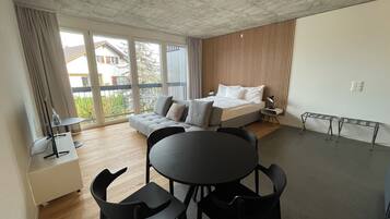 A modern bedroom with a bed, a small table, two chairs, a desk with a chair, and a balcony with curtains.