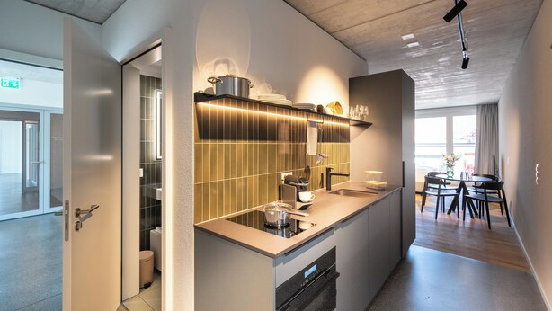 Una cocina moderna con horno empotrado, un lavamanos y una zona de comedor con mesa y sillas.