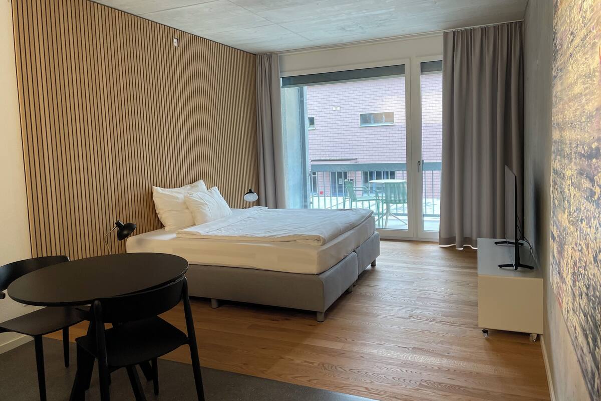 Una habitación de hotel moderna con una cama grande, un escritorio, una silla y un televisor.
