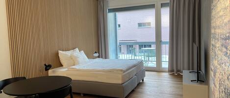 A modern hotel room with a large bed, a desk, a chair, and a TV.