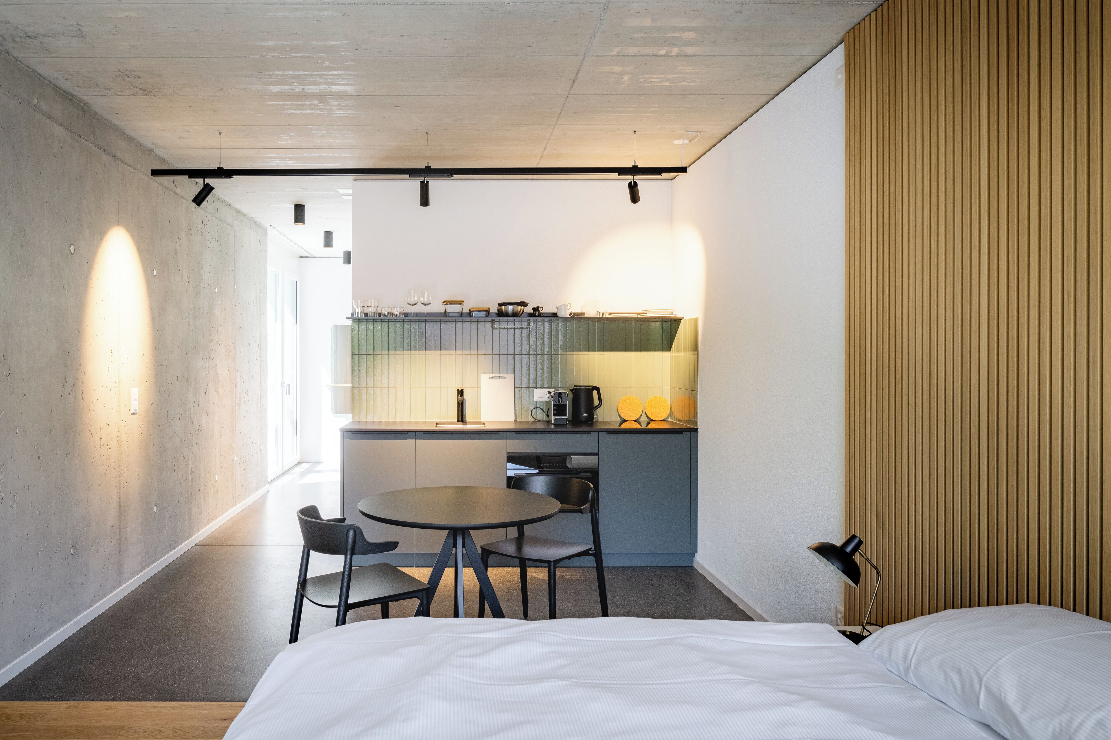 Une chambre d’hôtel compacte comprenant un lit, une petite table à manger avec des chaises, un coin cuisine et un mur décoratif en bois.