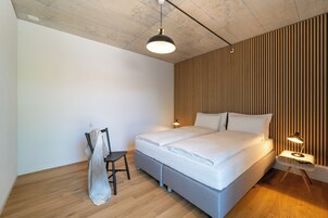 A modern bedroom with a large bed, a chair, and a bedside table with a lamp.
