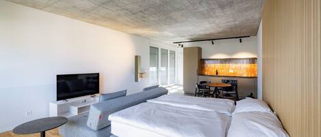 A modern hotel room with a large bed, a TV, a sofa, and a dining area.