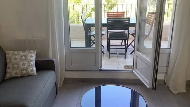 A room with a sofa, a small table, and a sliding glass door leading to an outdoor patio with chairs and a table. - 2 ROOM APARTMENT, SEMAPHORE, SAINTE MAXIME (Sainte-Maxime)