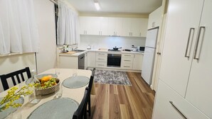 A compact kitchen with white cabinets, a dining table with chairs, and a small island with a sink and stove.