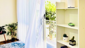 A room with a sliding glass door, a white air conditioning unit, a bookshelf with books and decorative items, and a blue patterned rug.