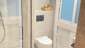 A modern bathroom with a glass shower enclosure, a white toilet, and a small sink. - Mikain Cathedral View (Donostia)