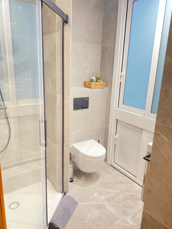 Une salle de bain moderne avec une douche à parois de verre, des toilettes blanches et un petit lavabo.