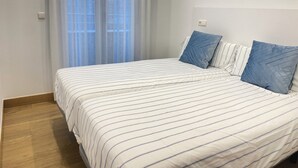 A neatly made bed with striped bedding, a window with sheer curtains, and a light switch on the wall. - Mikain Cathedral View (Donostia)