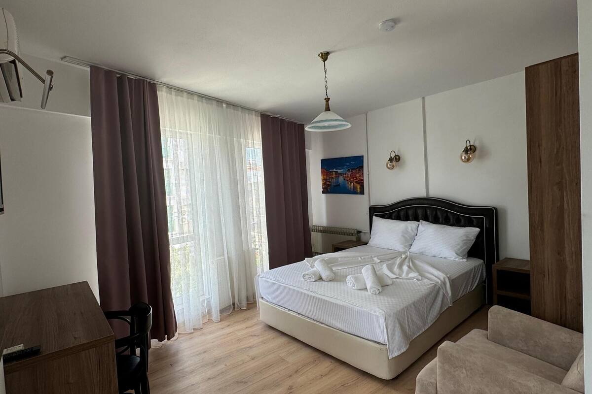 A bedroom with a bed, a desk, a chair, a sofa, and a painting on the wall.