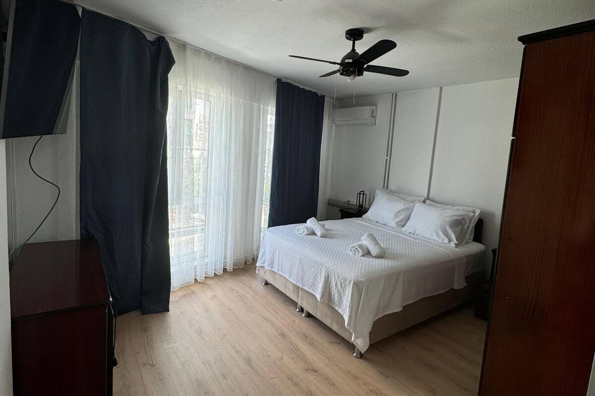 A bedroom with a bed, a ceiling fan, a desk, and a window with curtains.