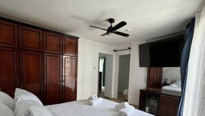 A bedroom with a large bed, wooden wardrobe, ceiling fan, and a television on a stand. - EDWIN CAFE BAR PANSIYON (Ayvalik)
