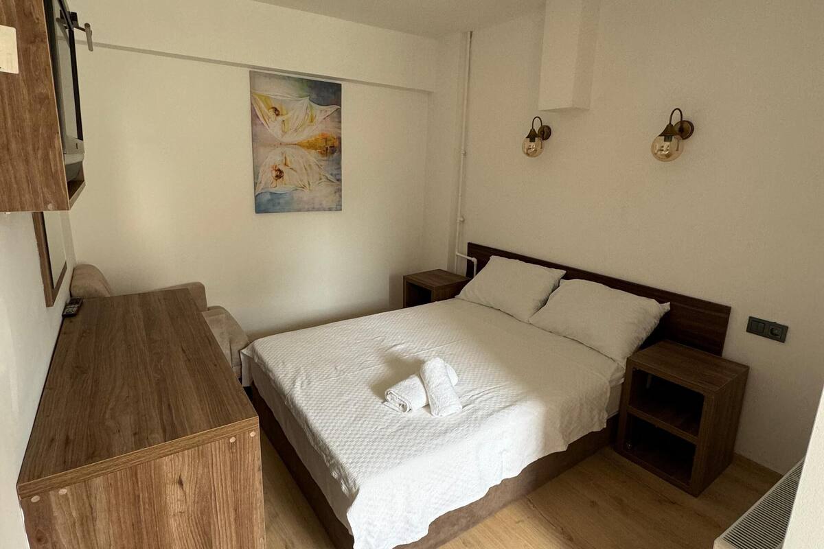 A bedroom with a wooden bed, a wooden dresser, a painting on the wall, and a small nightstand with a lamp.