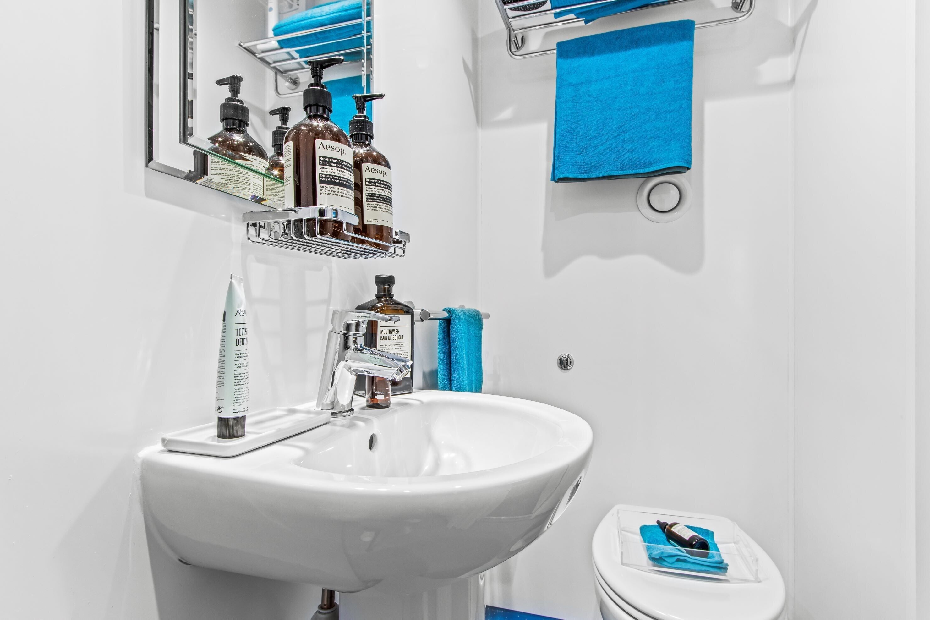 A bathroom with a white sink, a mirror, and toiletries on a shelf.