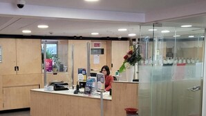 Een receptiebalie met een receptionist, een glazen scheidingswand en een bloemstuk.