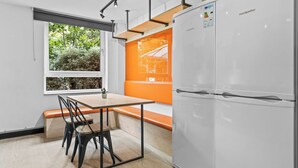 Een moderne keuken met een witte koelkast, een houten tafel met stoelen en een raam met uitzicht op bomen.