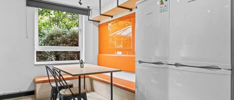 A modern kitchen with a white refrigerator, a wooden table with chairs, and a window with a view of trees.