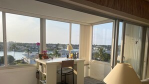 Een kamer met een bureau, een stoel, een lamp en uitzicht op water en gebouwen.
