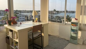 Een hoekappartement met bureau, stoel en grote ramen met uitzicht op een jachthaven.