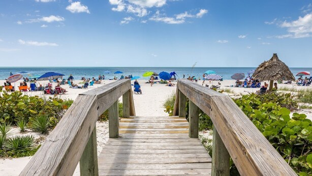 Een houten looppad dat naar een strand leidt, met parasols en mensen.