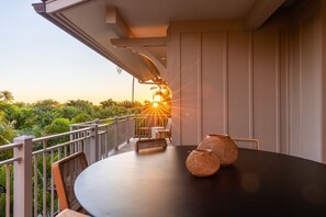 Un balcón con una mesa redonda y sillas de mimbre, con vistas a un jardín exuberante y palmeras.