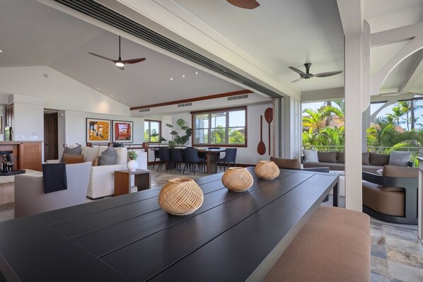 A modern living room with a long dark wooden table, three woven baskets, a sofa, and a dining area with chairs.