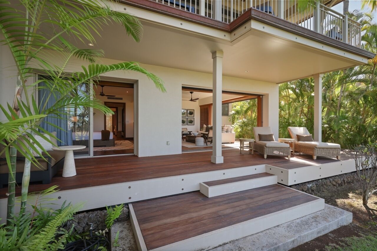 A modern house with a wooden deck, outdoor seating, and a view of the surrounding greenery.
