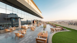 Una terraza en la azotea con mobiliario exterior, fachada de vidrio y vistas panorámicas de la ciudad.