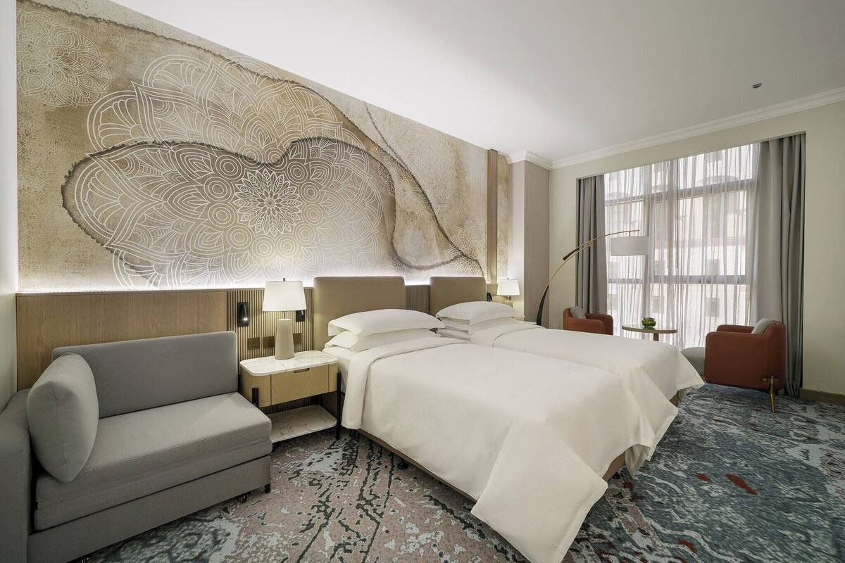 A hotel room with a large bed, a sofa, a desk, and a large window with curtains.