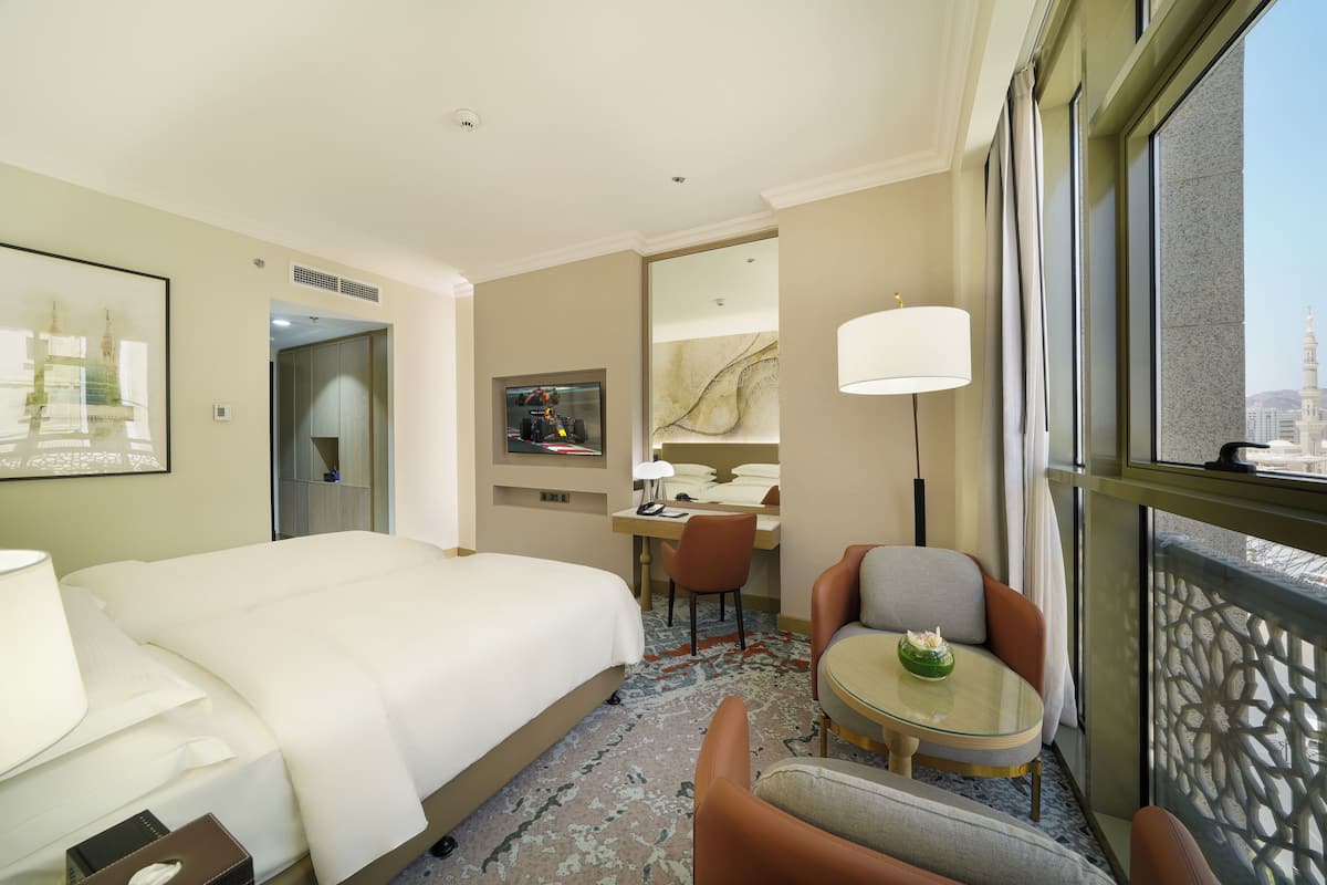 A hotel room with a large bed, a desk with a chair, a small round table, and a TV.