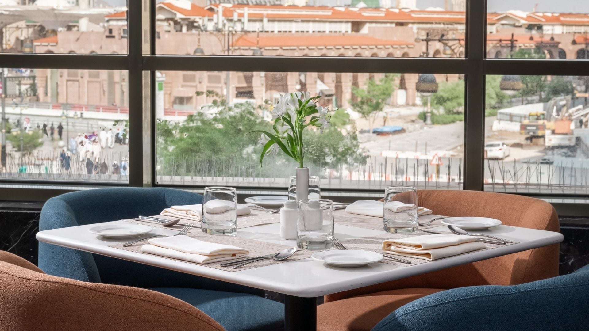 A dining table set for two with a vase of white flowers, glasses, and plates.
