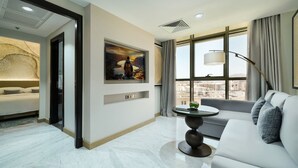 Habitación de hotel moderna con cama, sofá, mesa de comedor y un amplio ventanal con vistas a la ciudad.