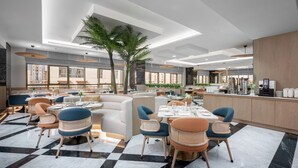 Un restaurante moderno con techos altos, una palmera en el centro y una variedad de opciones de asientos, incluyendo reservados y mesas.
