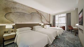 Una habitación de hotel con tres camas, un amplio elemento decorativo en la pared, un escritorio con lámpara y una silla.