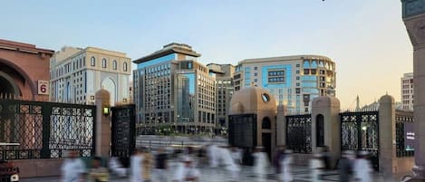 Uma praça pública com edifícios modernos, um grande guarda-sol e pessoas caminhando.