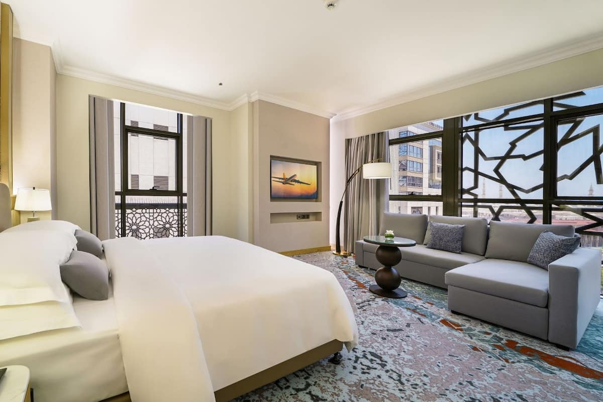 A hotel room with a large bed, a sofa, a TV, and a view of the cityscape.
