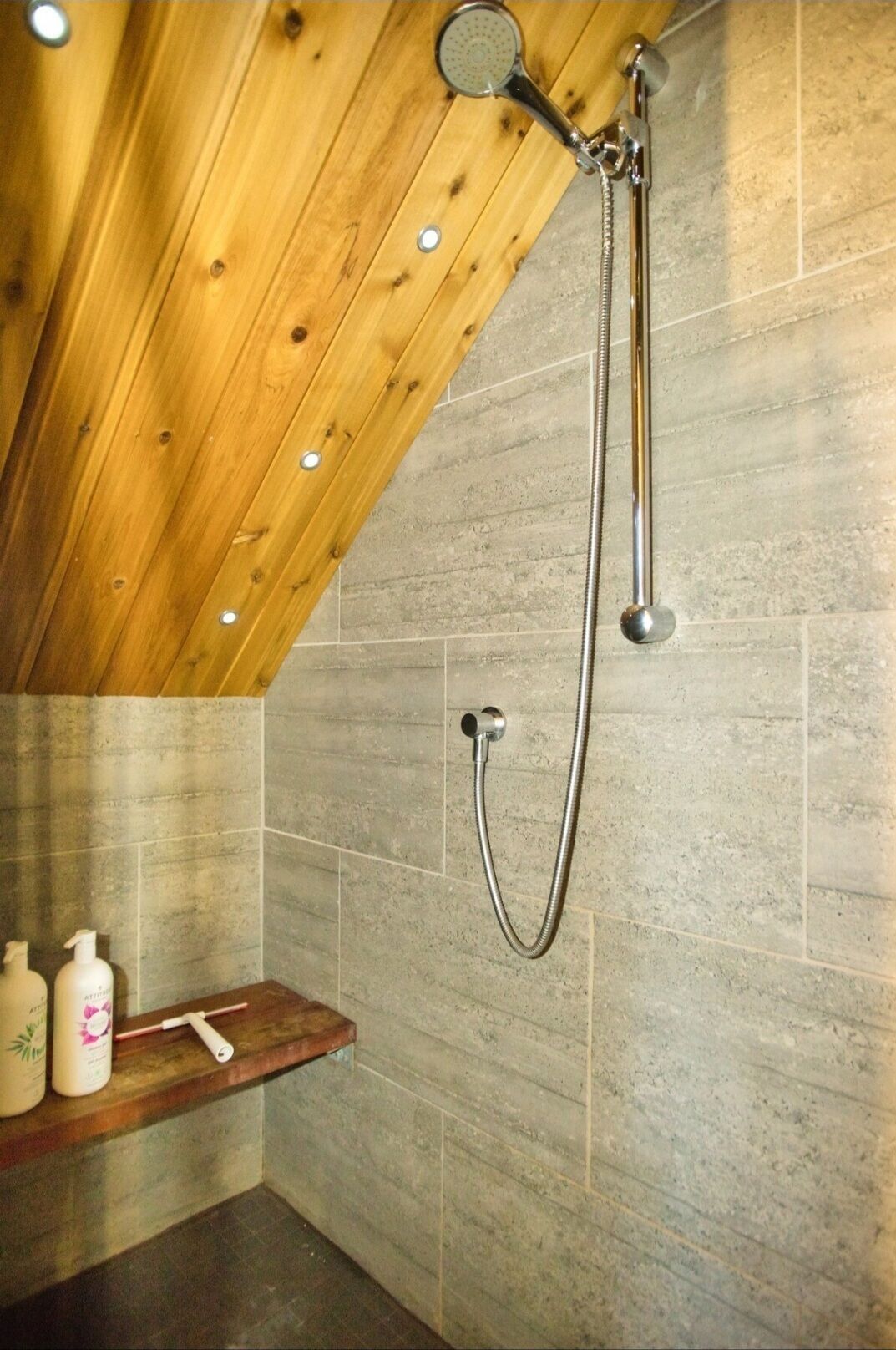 A shower with a wooden ceiling and stone tiles.