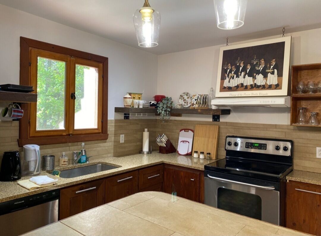Una cocina con gabinetes de madera, una estufa de acero inoxidable, un lavamanos doble y una ventana con vistas al verdor.