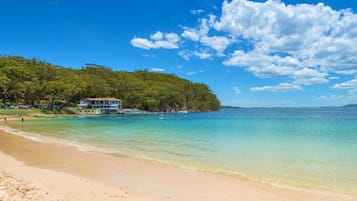 A beach with clear turquoise water, a sandy shore, and a building with a balcony overlooking the sea.