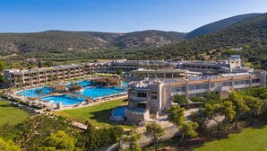 Un hotel a tema castello con diverse piscine, una vegetazione lussureggiante e montagne sullo sfondo.