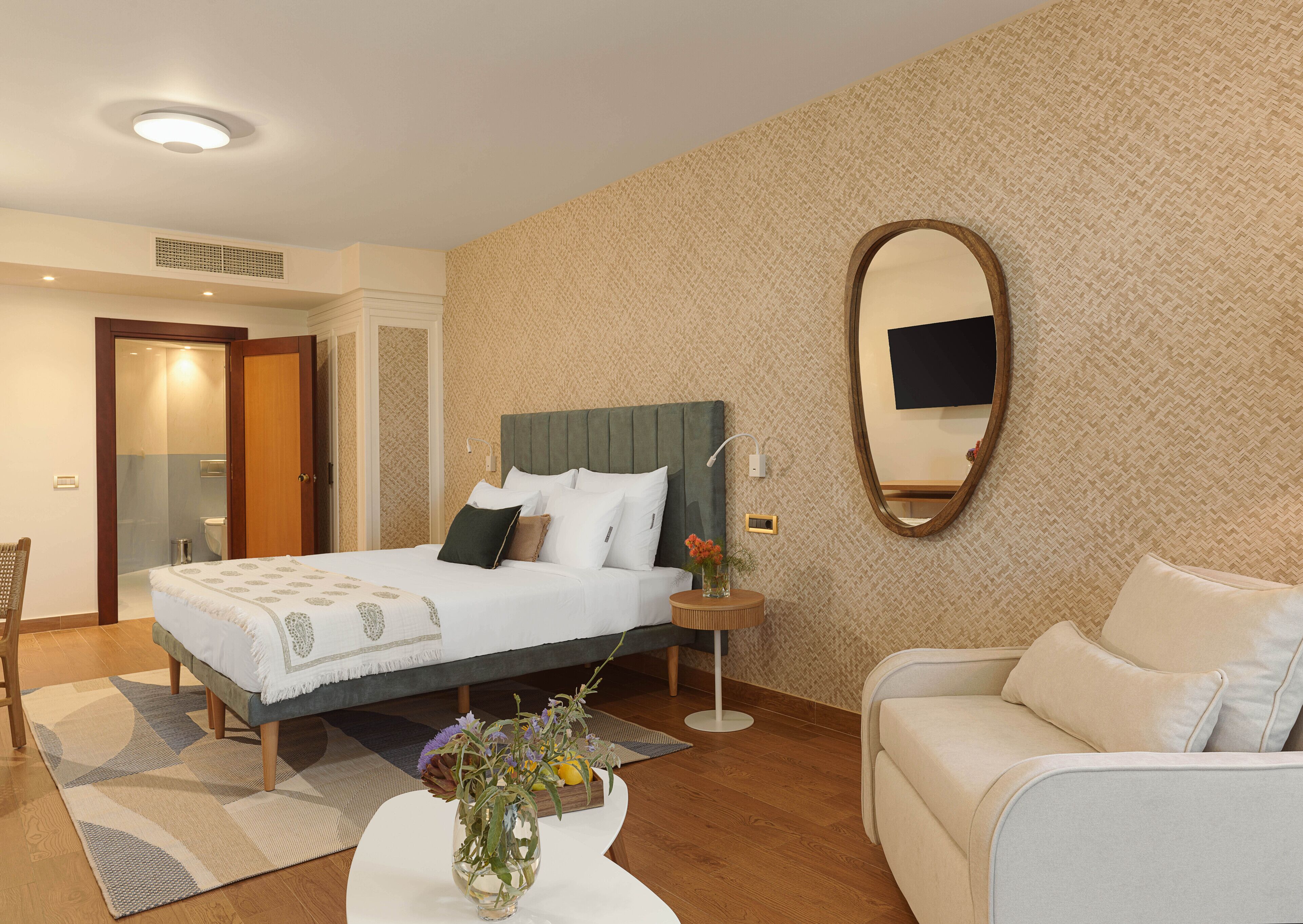 Une chambre d’hôtel comprenant un lit, un coin salon avec un canapé, une table basse ronde et un miroir au mur.