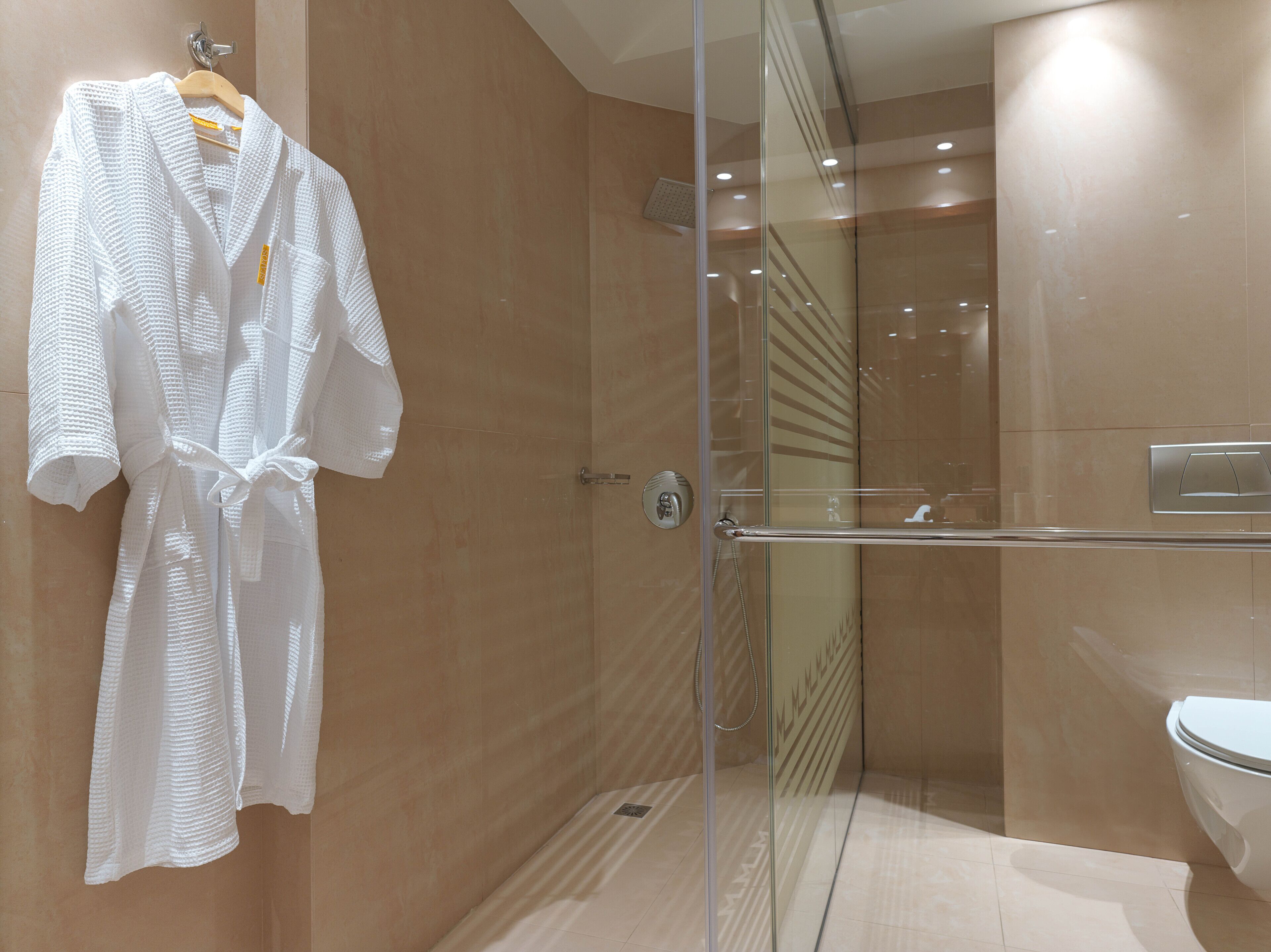 A modern bathroom with a glass-enclosed shower, a white bathtub, and a towel rack with a white bathrobe.