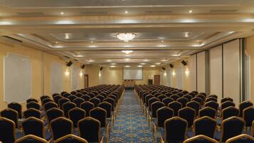 A conference room with rows of chairs, a projector screen, and a large chandelier.