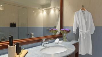 Une salle de bain avec un grand miroir, un lavabo, un plateau en bois avec une brosse, et une robe accrochée au mur.